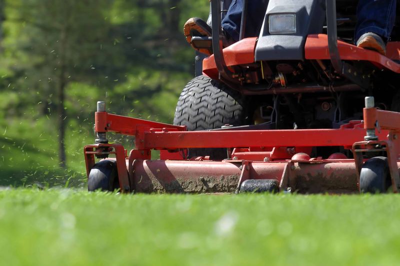 Close-up of a riding mower deck cutting grass, clippings flying from under the blade