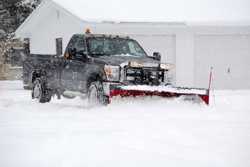 Plow truck clearing snow from a commercial driveway and parking area