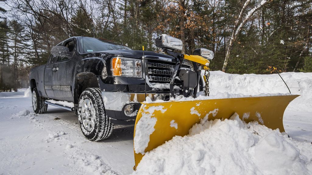 Plow truck pushing a heavy load of snow across a commercial parking lot in winter